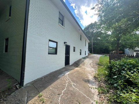A white building with a black door and windows is surrounded by greenery.