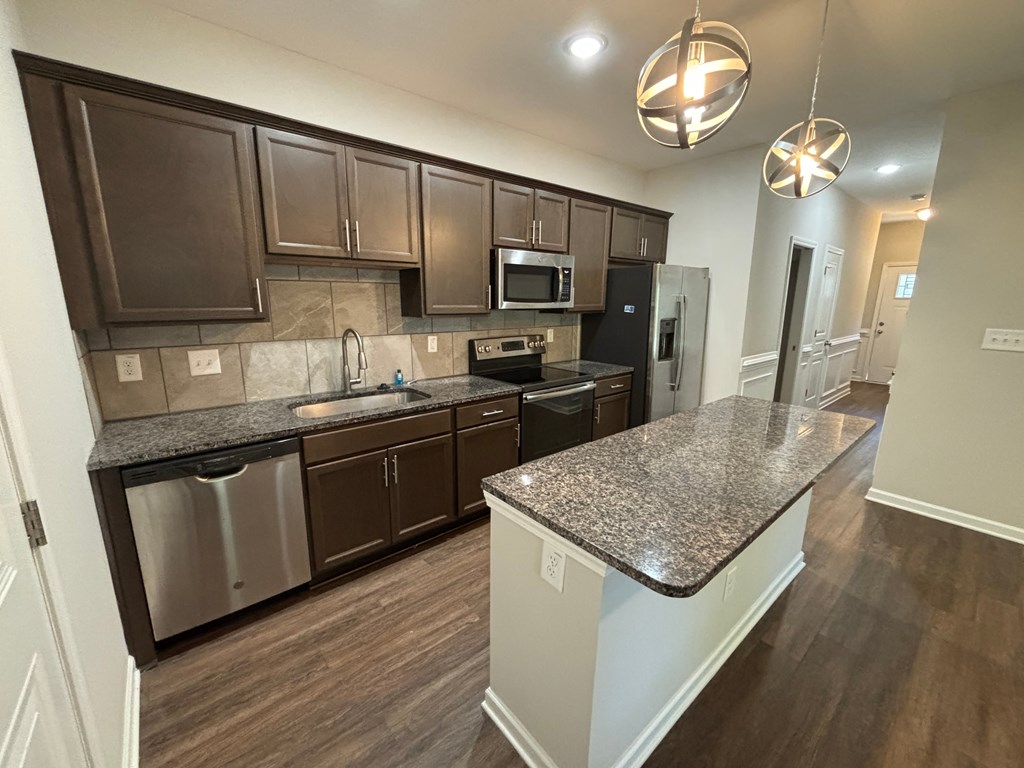 A kitchen with dark brown cabinets and granite countertops.