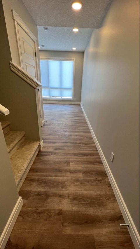 a hallway with wood floors and stairs and a window