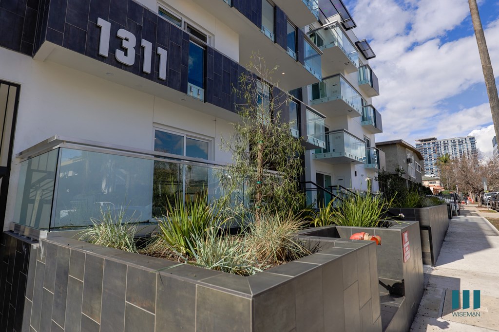 an apartment building with a sidewalk and plants in front of it