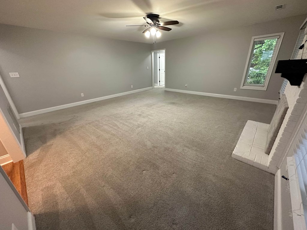a empty living room with carpet and a ceiling fan