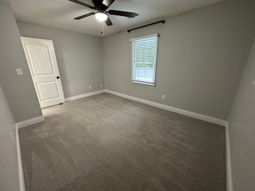 a empty living room with carpet and a ceiling fan