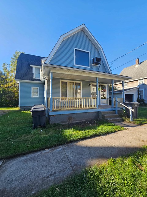 A blue house with a porch and a trash can in front.