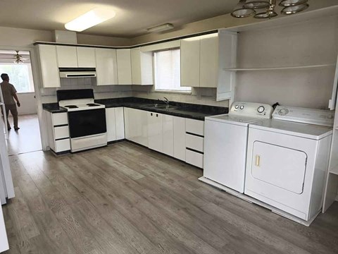 A man is standing in a kitchen with white cabinets and a black countertop.
