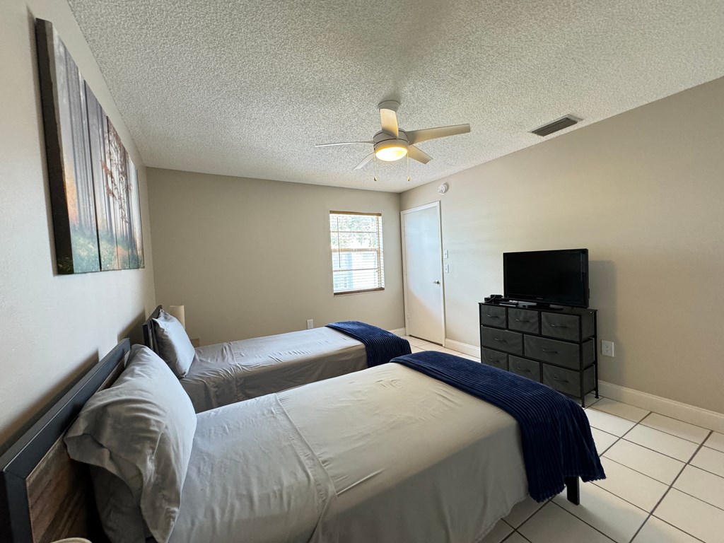 two beds in a bedroom with a ceiling fan and a tv
