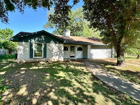 A green and white house with a tree in front.