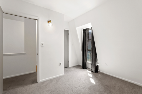 a living room with white walls and carpet and a door to a closet and a