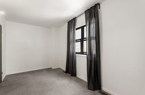 an empty room with white walls and a window with black curtains