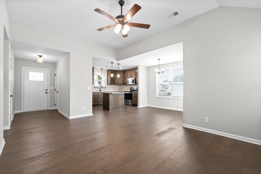 an empty living room with a ceiling fan and a kitchen