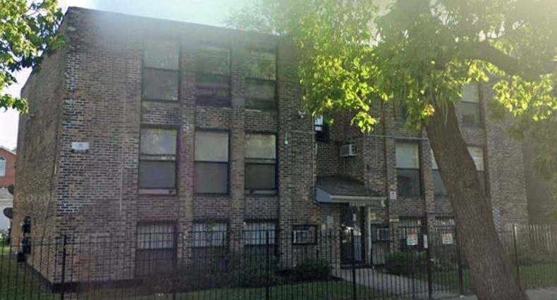 A brick building with a black fence and a tree in front.