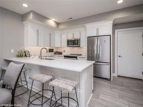 A kitchen with white cabinets and a white island with three barstools.