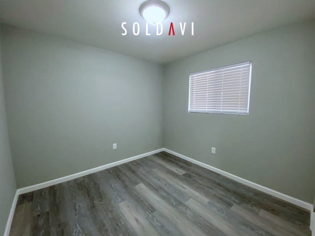A room with wooden flooring and a window with blinds.