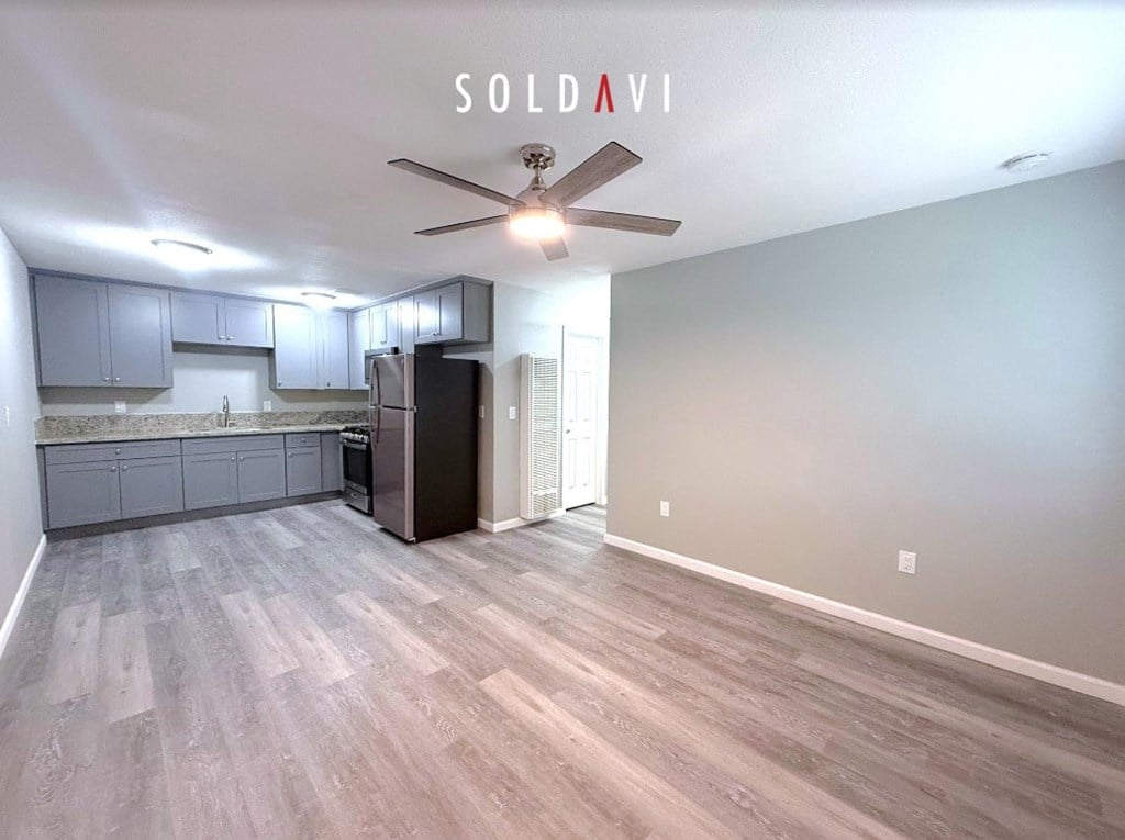 A room with a ceiling fan and a kitchen area with a refrigerator.