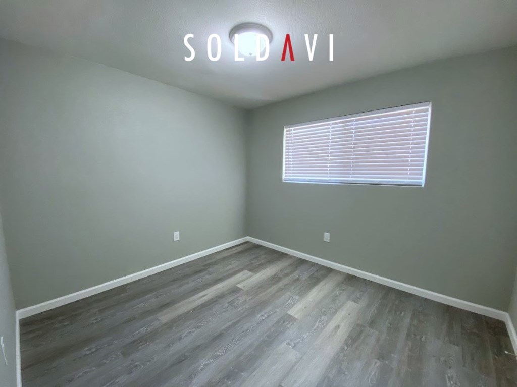 A room with wooden flooring and a window with blinds.