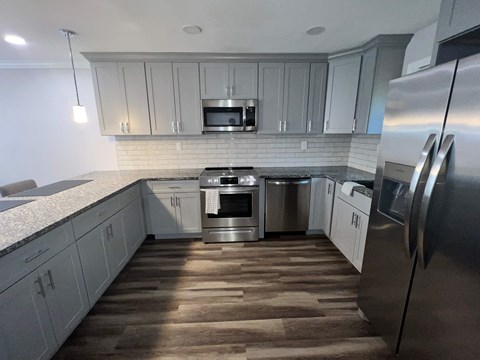 A modern kitchen with a stainless steel refrigerator and wooden flooring.