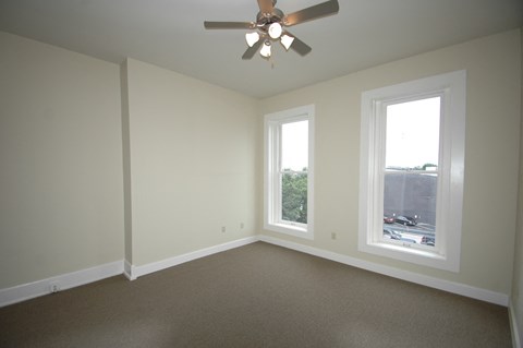 an empty living room with a ceiling fan and two windows