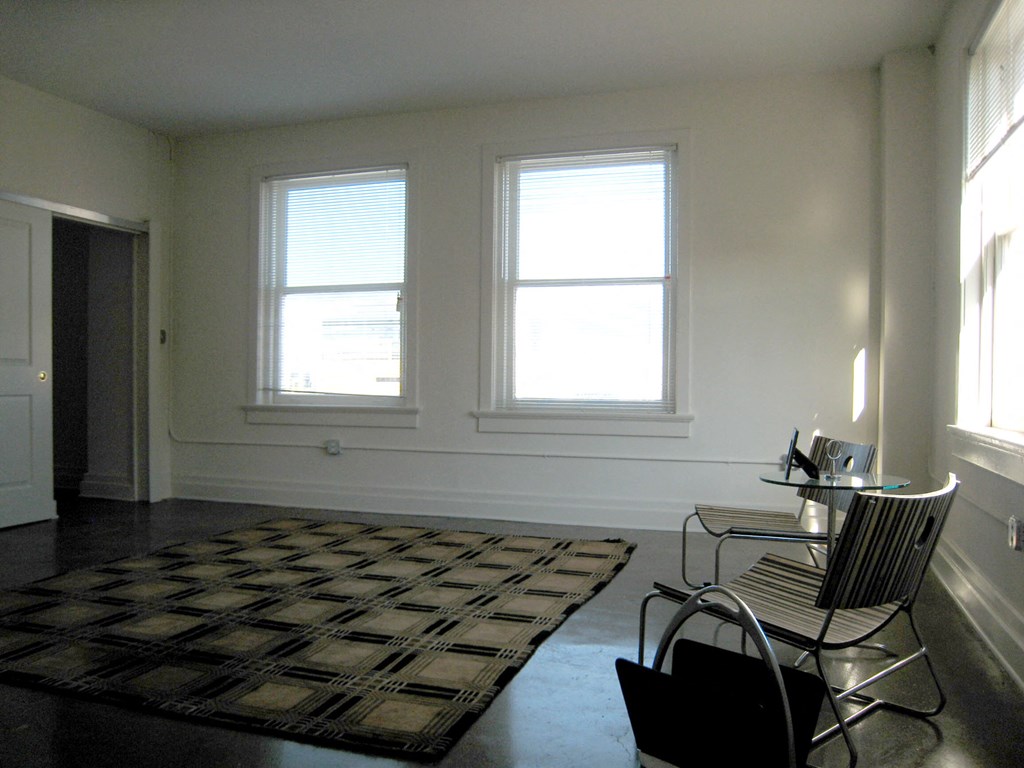 a living room with chairs and a rug and three windows
