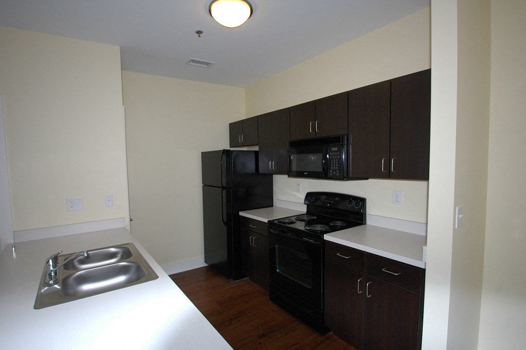 a kitchen with black appliances and white countertops in an empty apartment