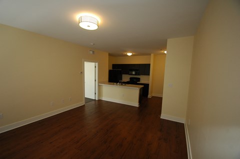 an empty living room with wood floors and a kitchen