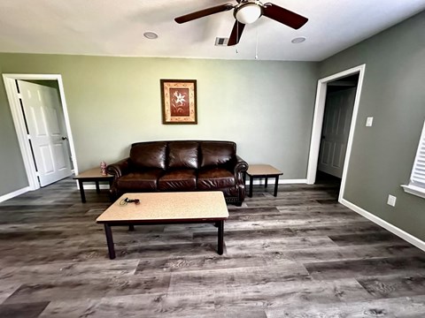 A brown leather couch sits in a room with a ceiling fan.