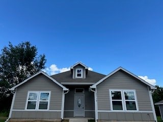 A grey house with a brown roof and a white door.