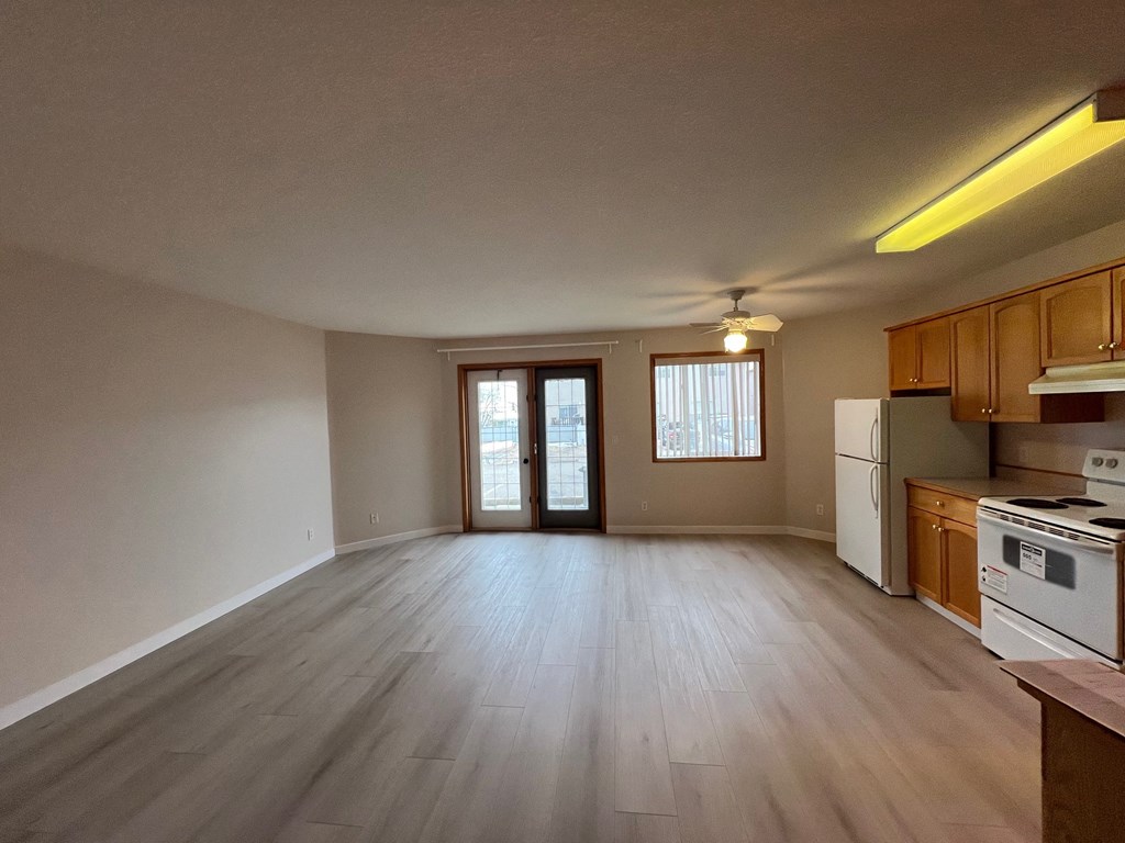 an empty living room and kitchen with wood flooring and white appliances