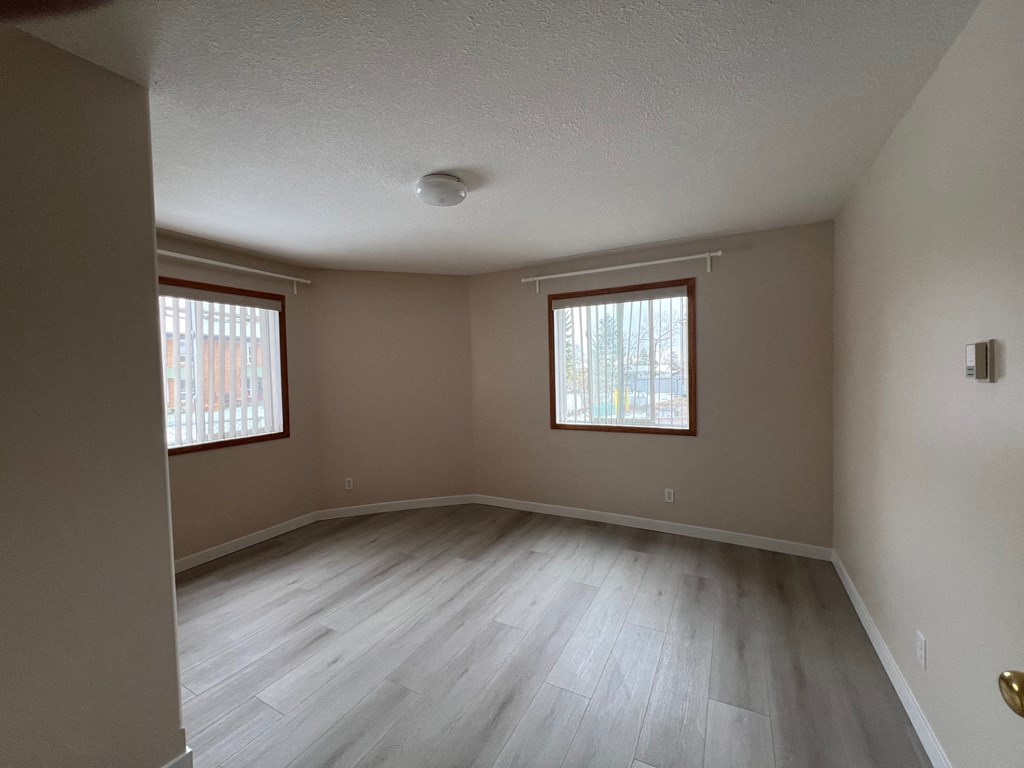 an empty living room with wooden floors and two windows