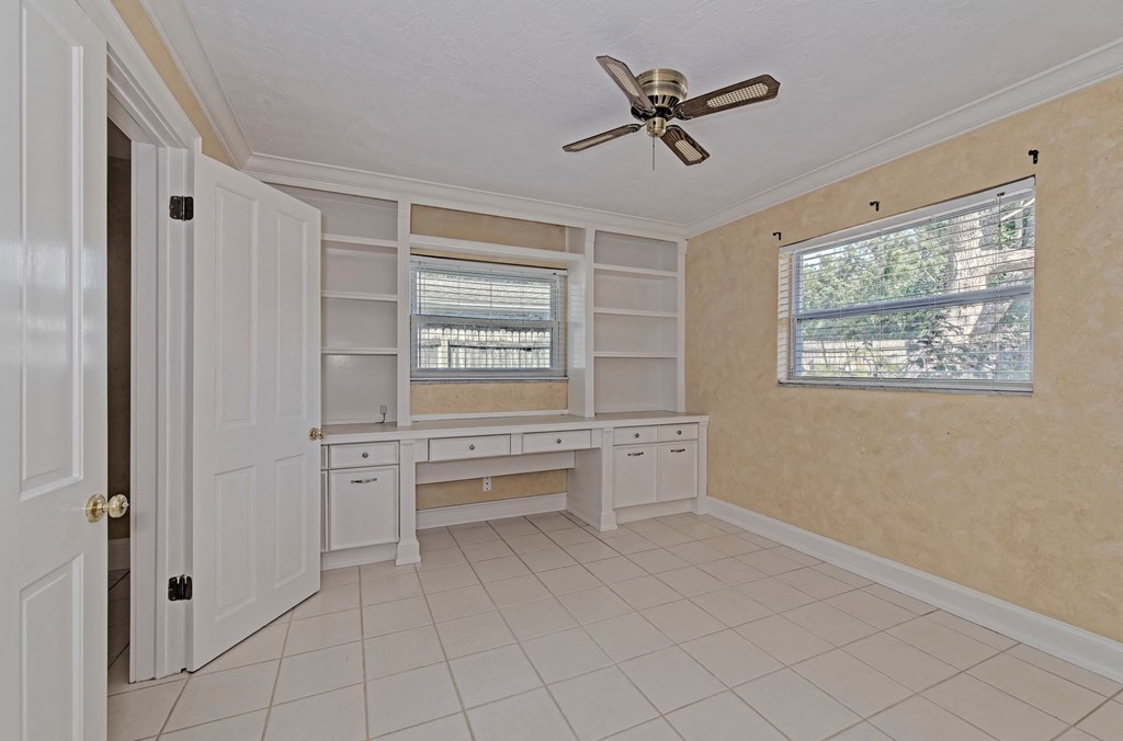 a room with a desk and a window and a ceiling fan