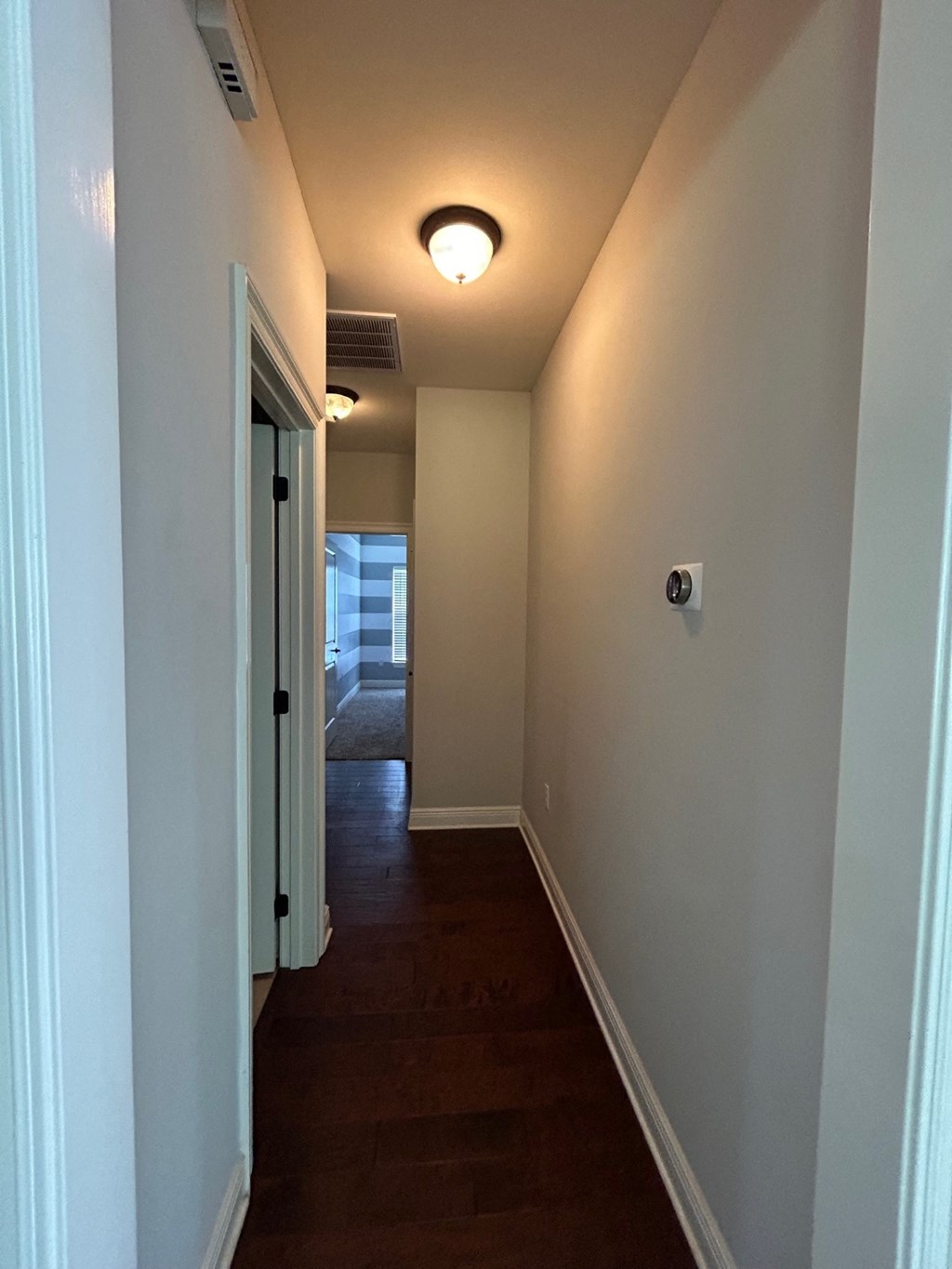 a hallway with a wood floor and white walls and a ceiling light