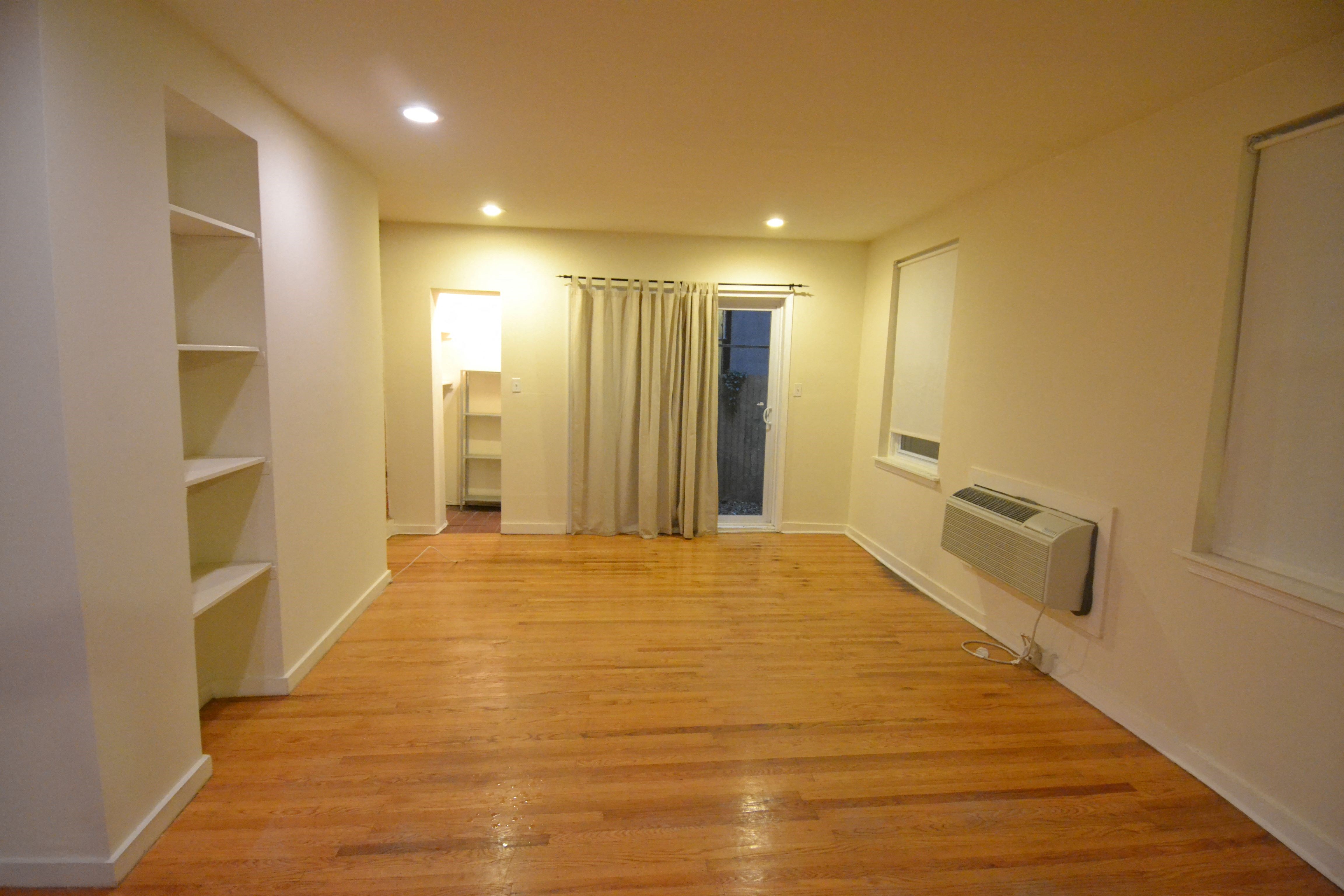 a living room with a wooden floor and a hallway with shelves and a curtain