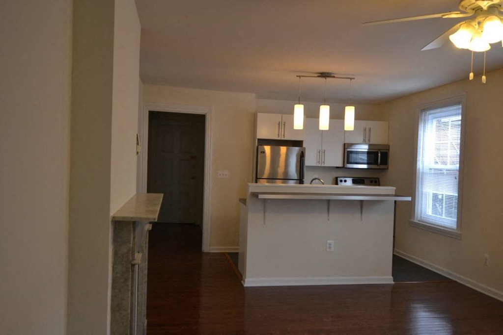 an empty living room with a kitchen and a ceiling fan