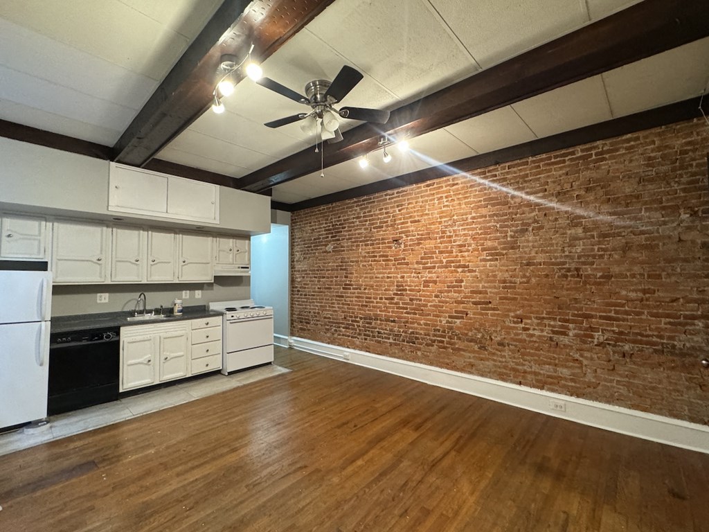 an empty living room with a brick wall and a kitchen