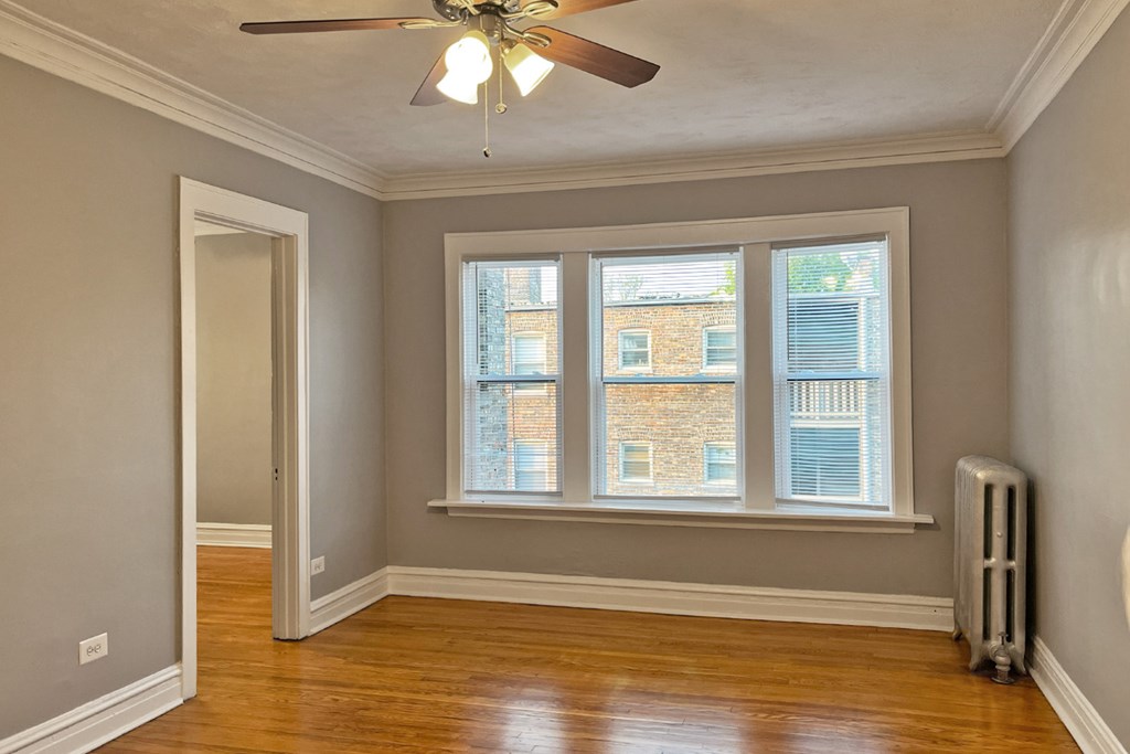 A room with a ceiling fan and a window with a view of a building outside.