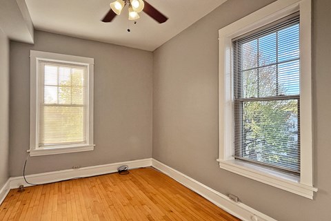 A room with a ceiling fan and two windows.
