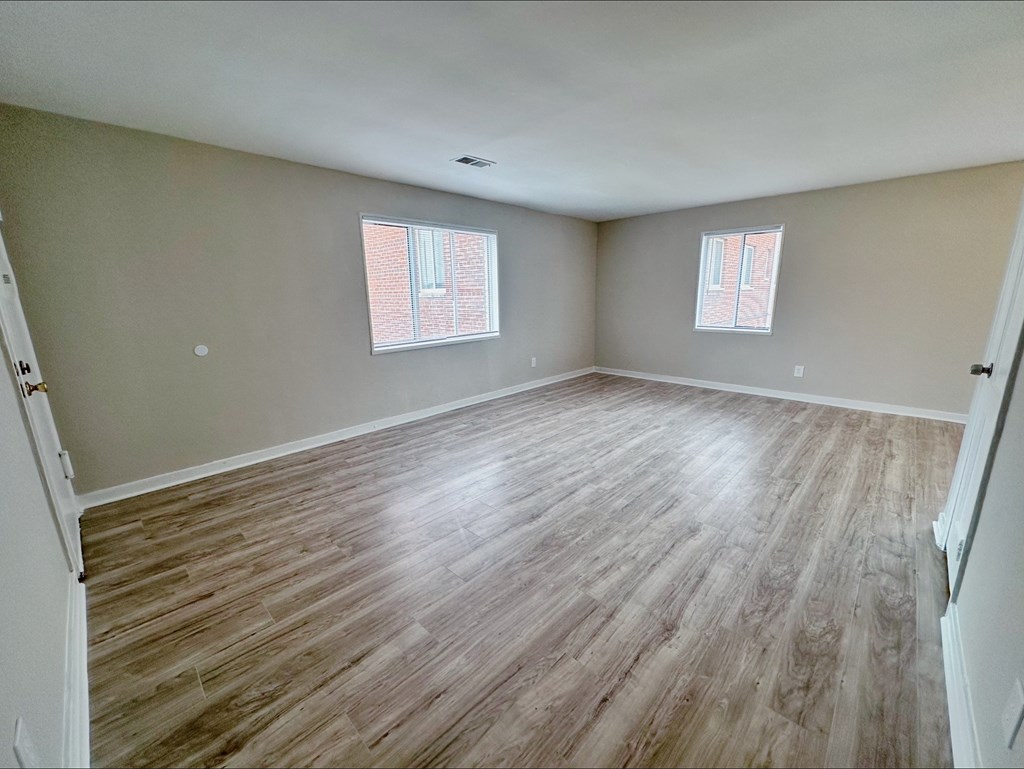 A room with wooden flooring and two windows.