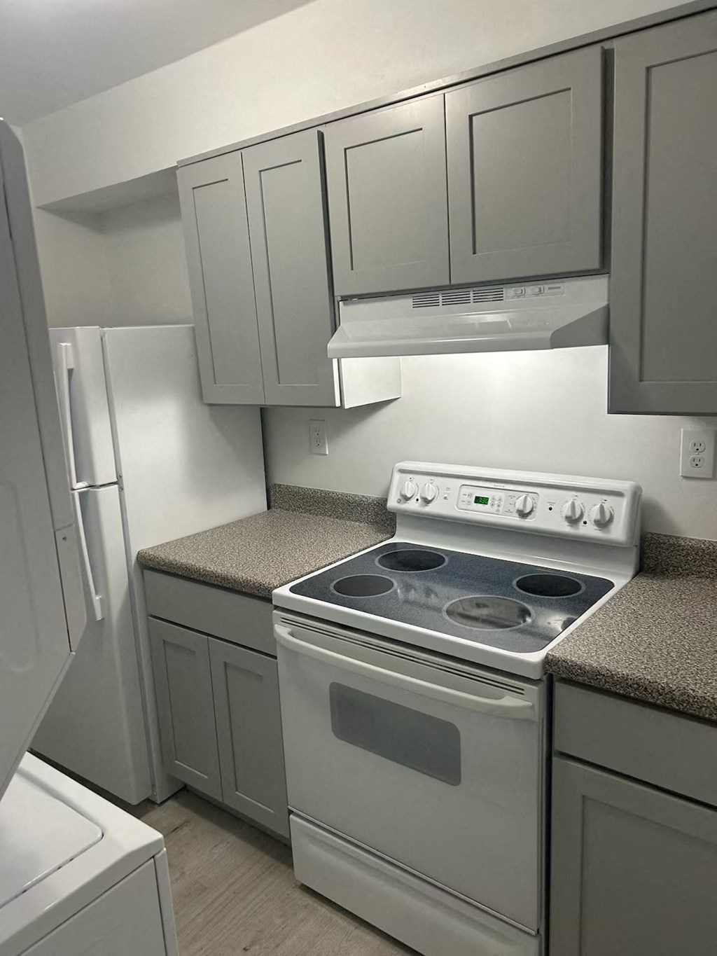 A white stove top oven with four burners and a white refrigerator in a kitchen.