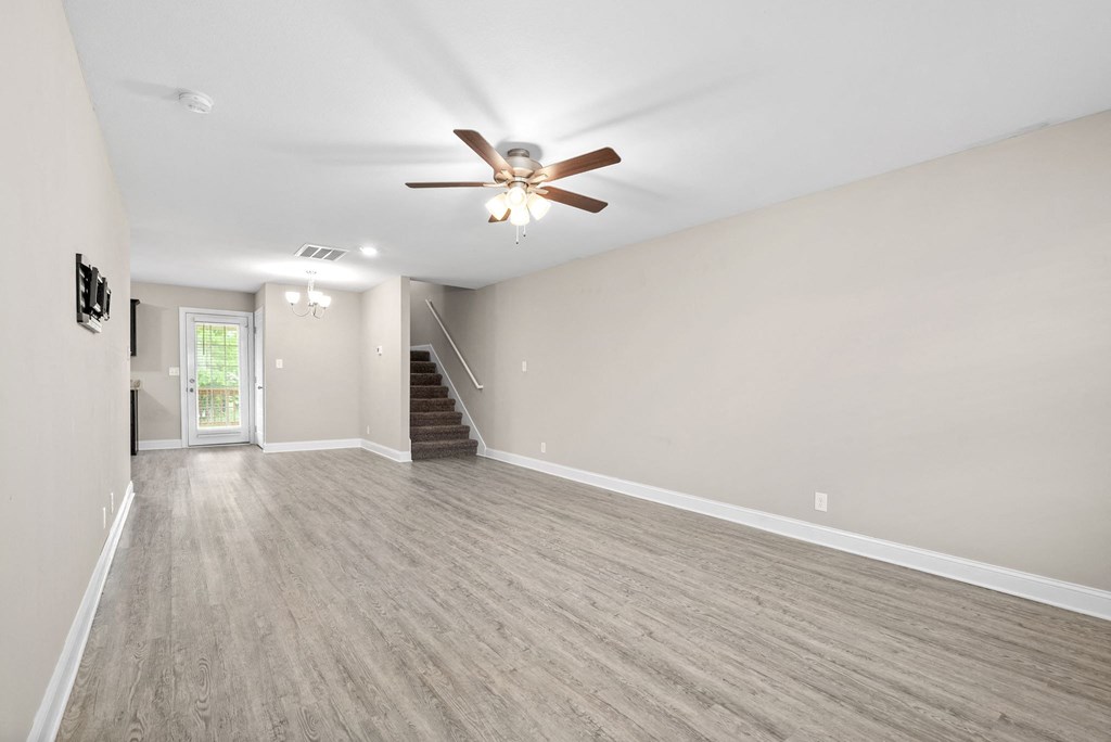 an empty living room with a ceiling fan and a staircase