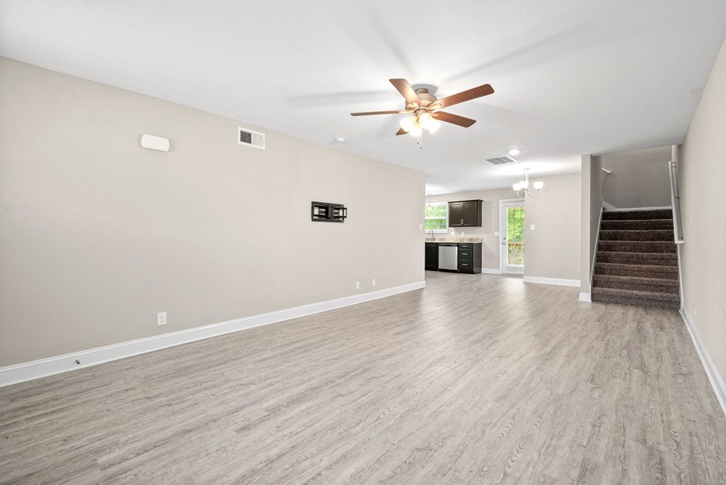 an empty living room with a ceiling fan and a staircase