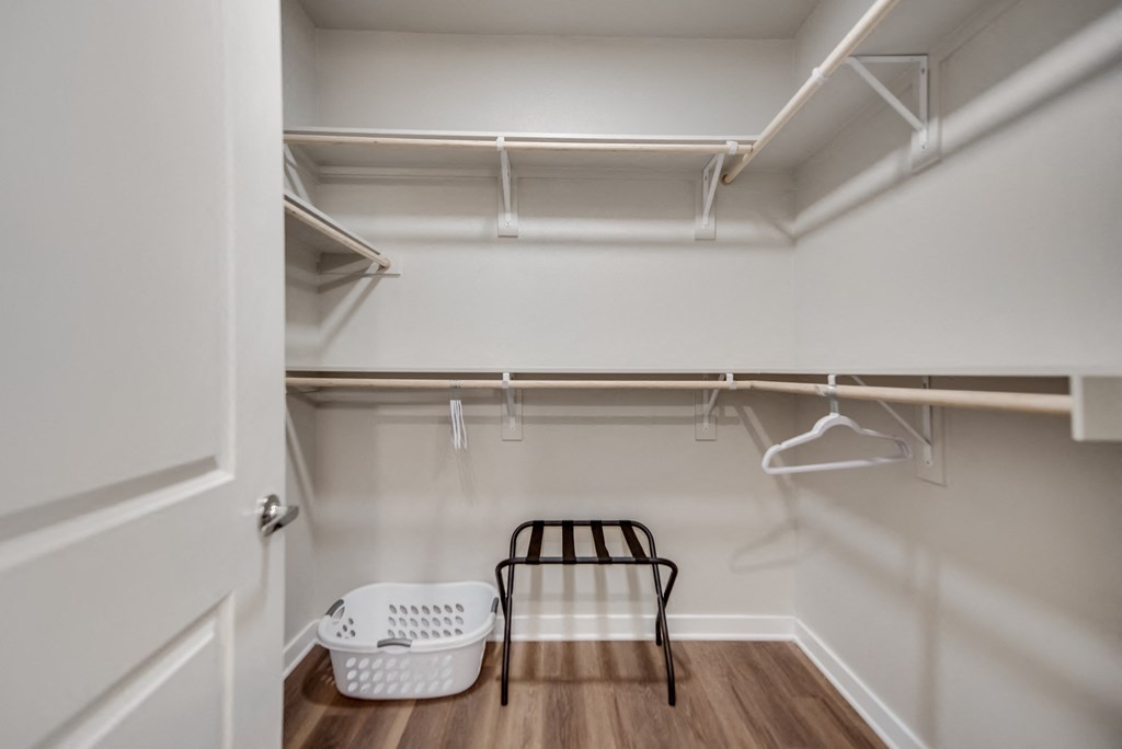 a walk in closet with white walls and a white closet organizer with a black stool