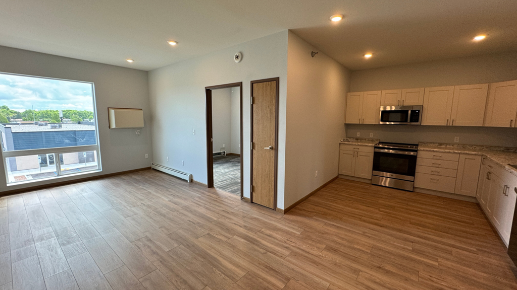 an empty living room with a large window and a kitchen