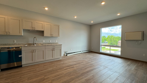 an empty living room with a kitchen and a large window