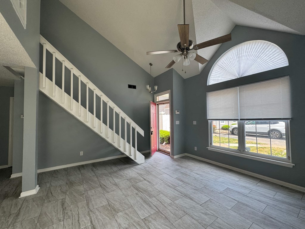 a large empty living room with a staircase and a ceiling fan