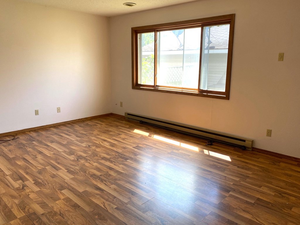 an empty living room with wood flooring and a window