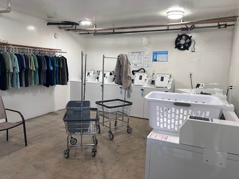 A laundry room with a washer and dryer, a chair, and a rack of clothes.