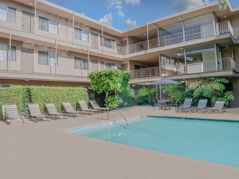 A pool surrounded by lounge chairs and umbrellas in front of a building.