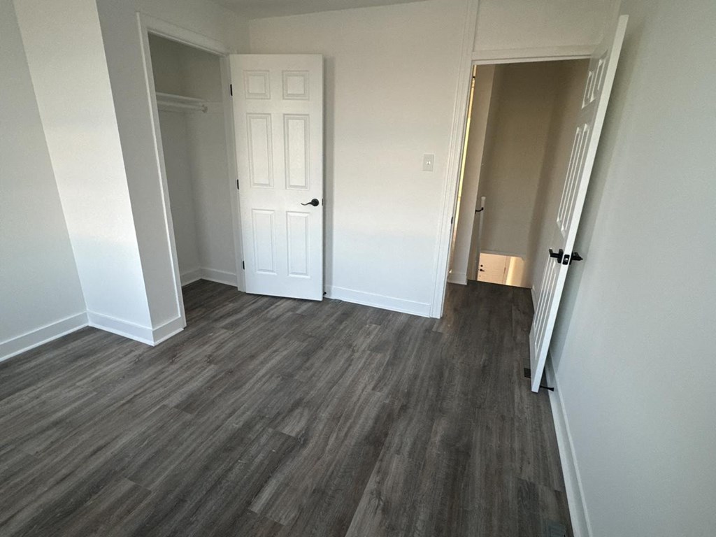 a bedroom with a door and a hallway with wood flooring