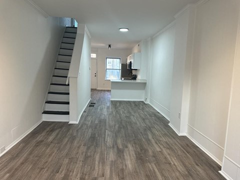 an empty living room with a staircase and a kitchen