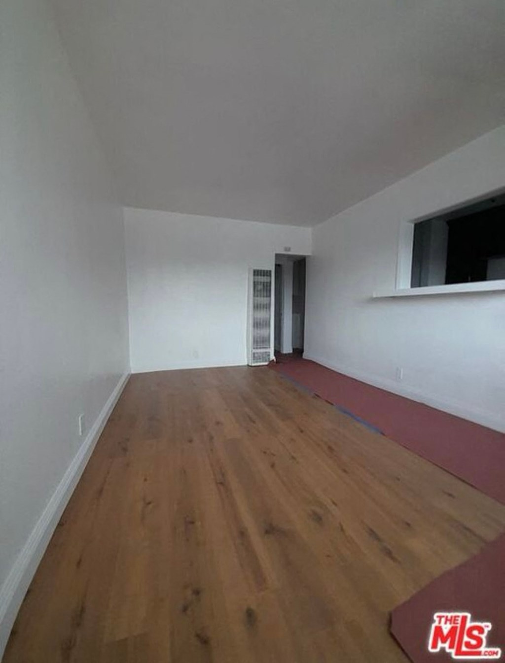 a room with a wood floor and white walls and a window
