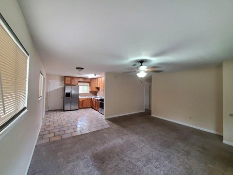 an empty living room with a kitchen in the background