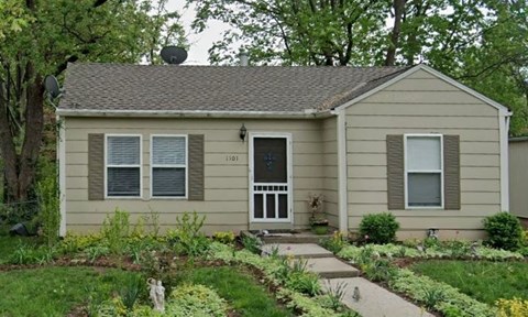 a small tan house with a garden in front of it